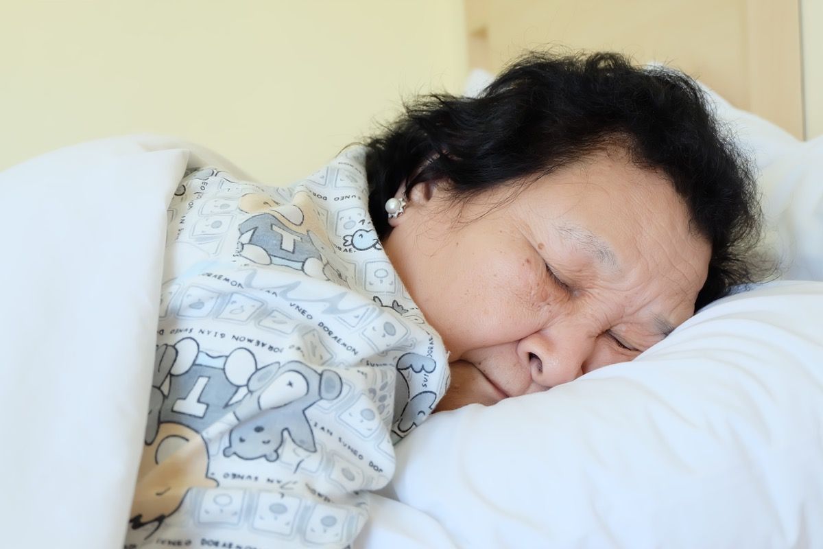Ηλικιωμένη ασιατική γυναίκα που κοιμάται στο PJS με το κεφάλι στο μαξιλάρι