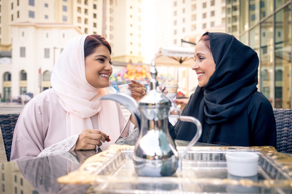 Dvě ženy na sobě hidžáby - jedna růžová a jedna černá - sdílejí čaj venku