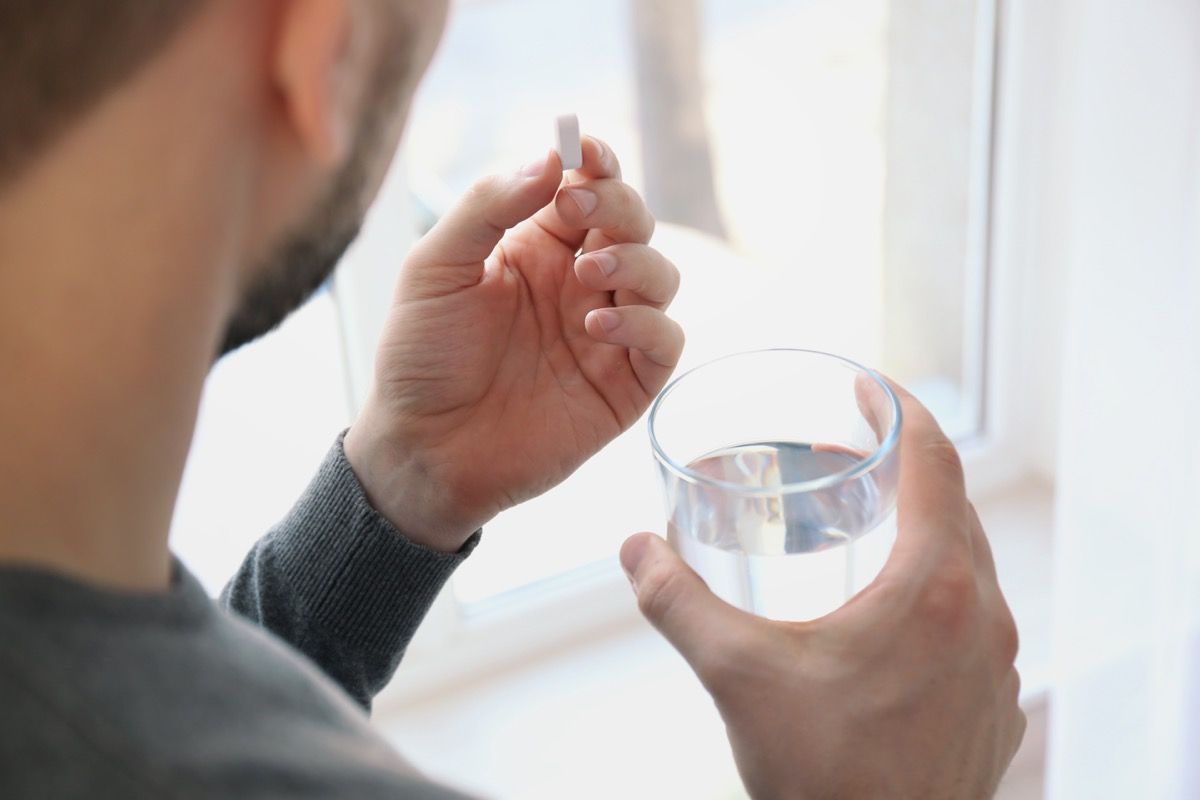 Človek jemlje tableto s kozarcem vode
