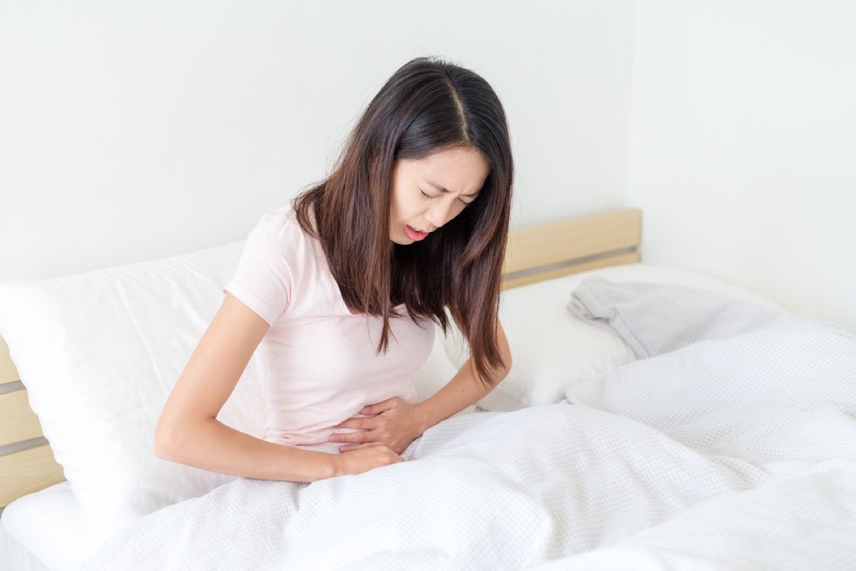 femeie tânără cu dureri de stomac ghemuit în pat, simptome de stomac
