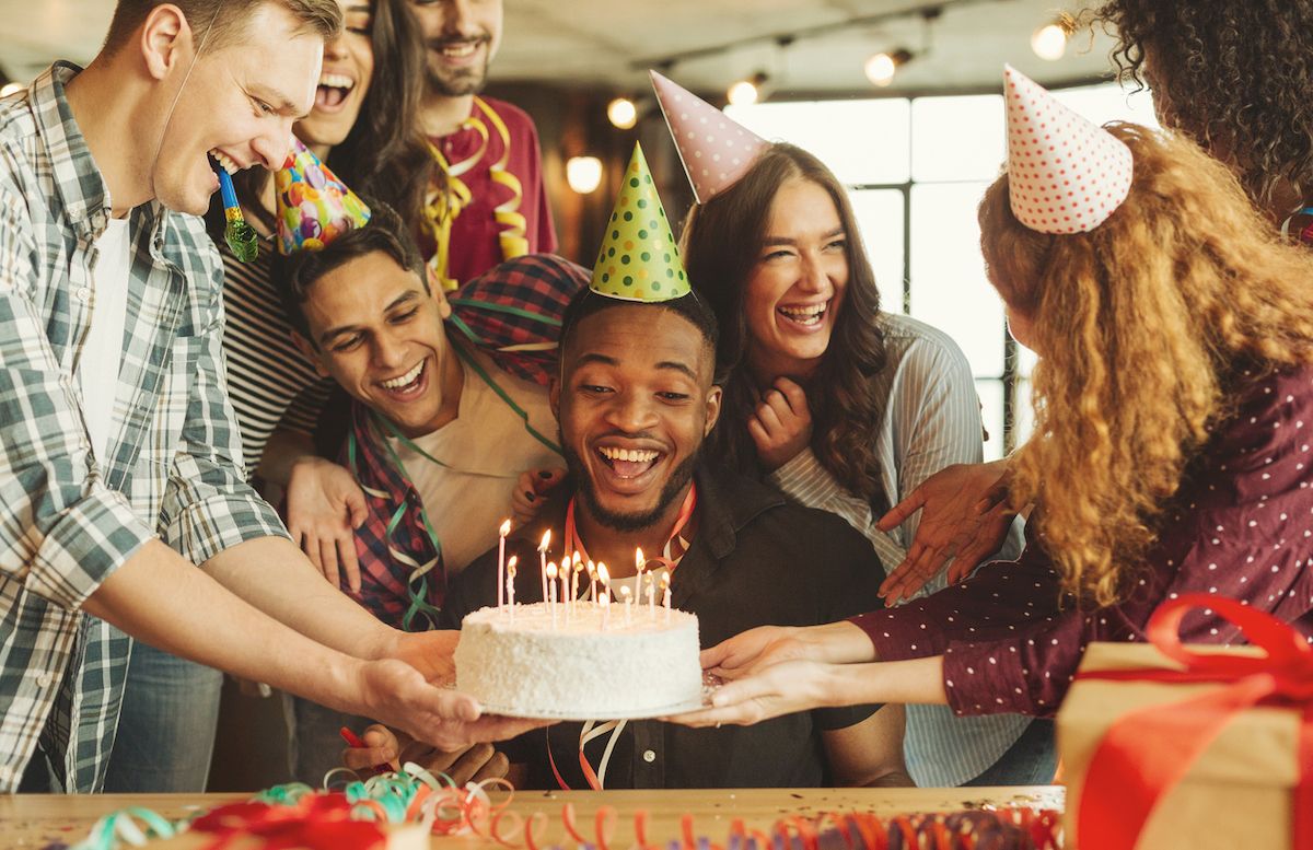 Laimingas juodaodis, švenčiantis savo gimtadienį, žiūrintis į tortą su žvakėmis, draugų apsuptyje