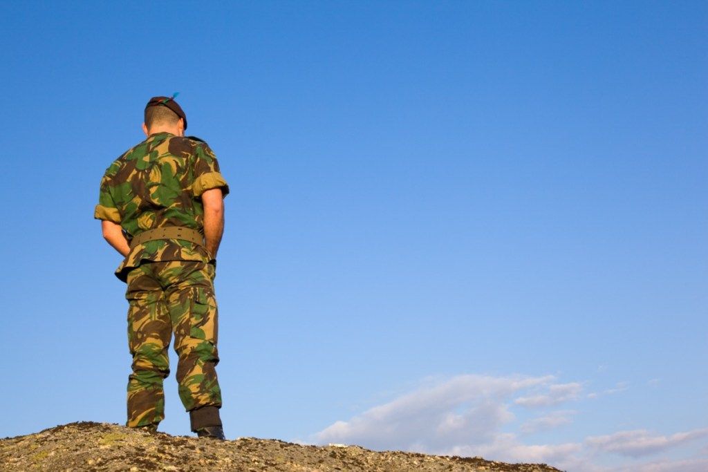 militāra cilvēka mugura stāv un skatās uz leju