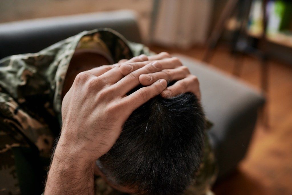 militārs cilvēks apsēžas ar galvu rokās