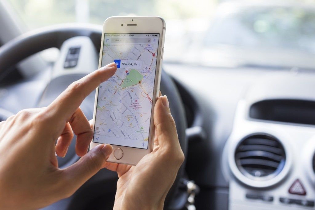 moteris su obuolių žemėlapiais telefone ir automobilyje