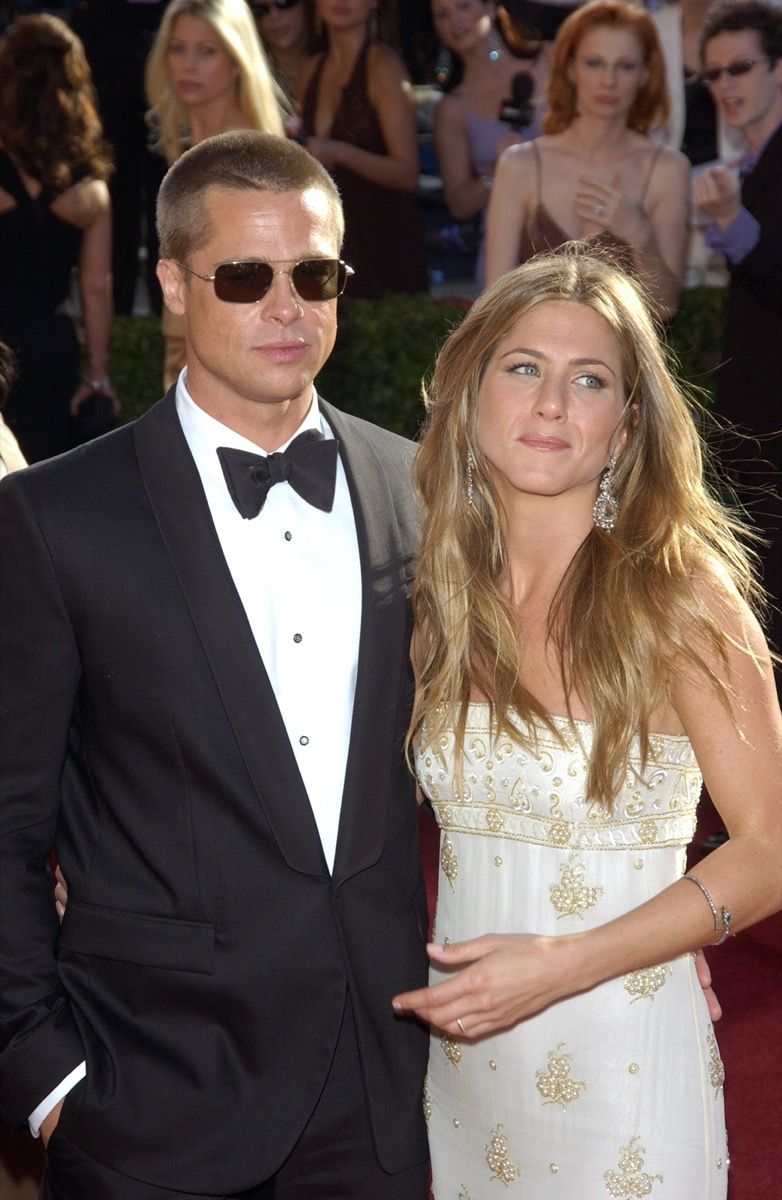 Jennifer Aniston mengenakan gaun putih dan Brad Pitt mengenakan setelan hitam di karpet merah di The Emmy Awards pada tahun 2004