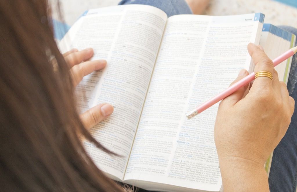 Femeie care citește și răsfoiește dicționarul, origini comune ale cuvintelor