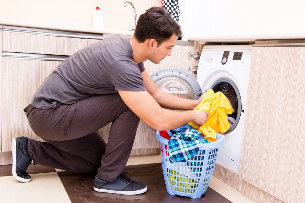 Мужчина кладет одежду в стиральную машину