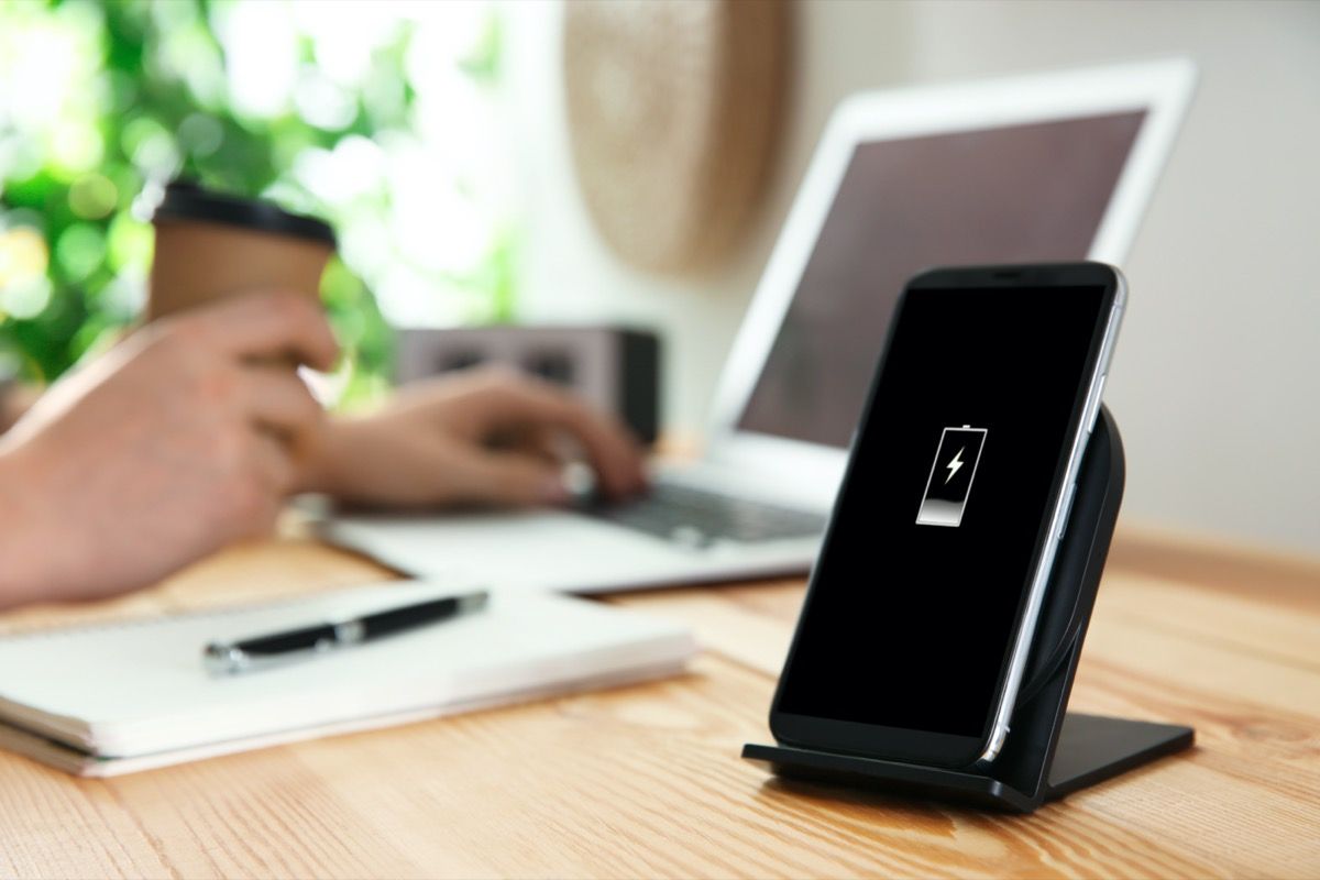 Chargeur de téléphone contact noir sur un bureau en bois à côté de personne travaillant sur un ordinateur portable