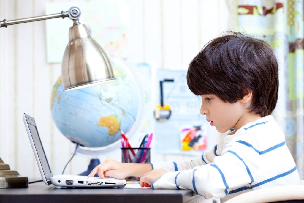 Детето, което прави домашното си на компютър, начините за връщане в училище е различно