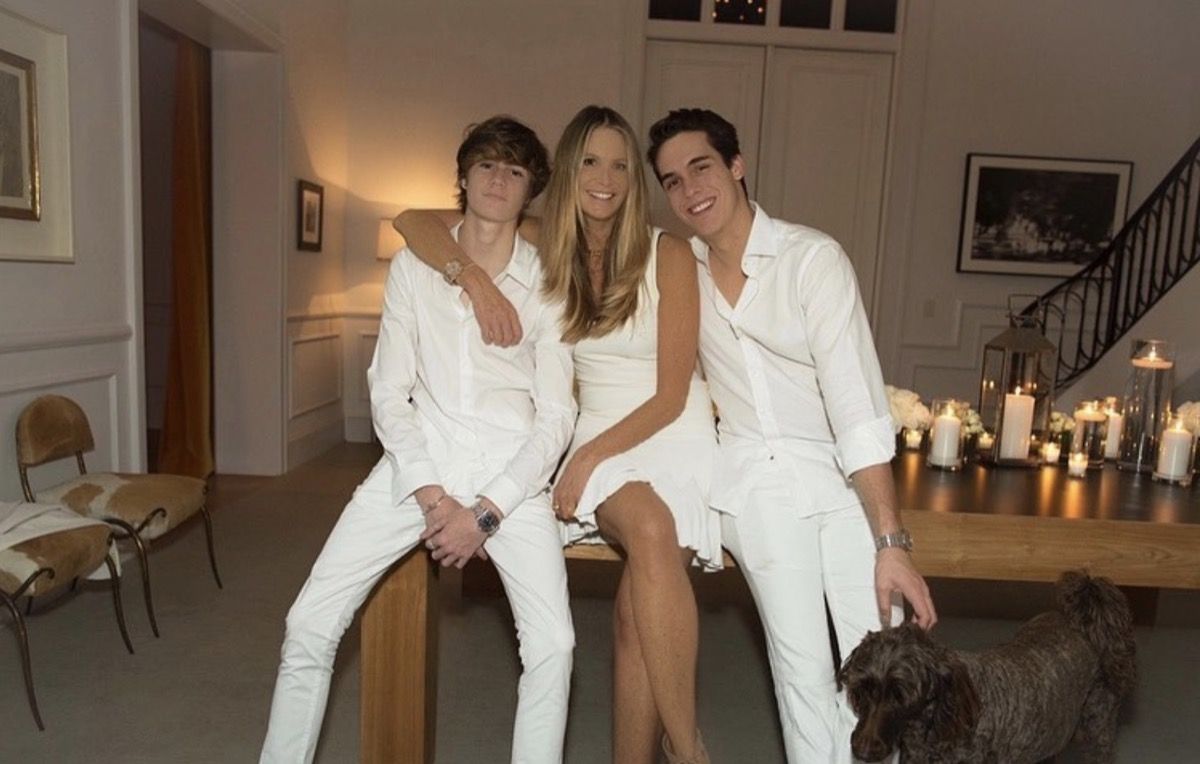 Elle Macpherson y sus dos hijos vestidos de blanco y sentados en una mesa junto a un perro marrón