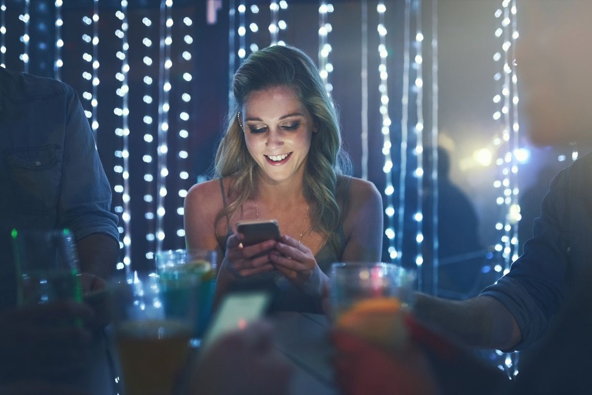Aufnahme einer jungen Frau, die auf ihrem Smartphone eine SMS schreibt, während sie in einem überfüllten Nachtclub sitzt