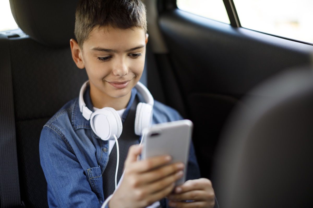 pusaudzis zēns automašīnā izmanto mobilo tālruni