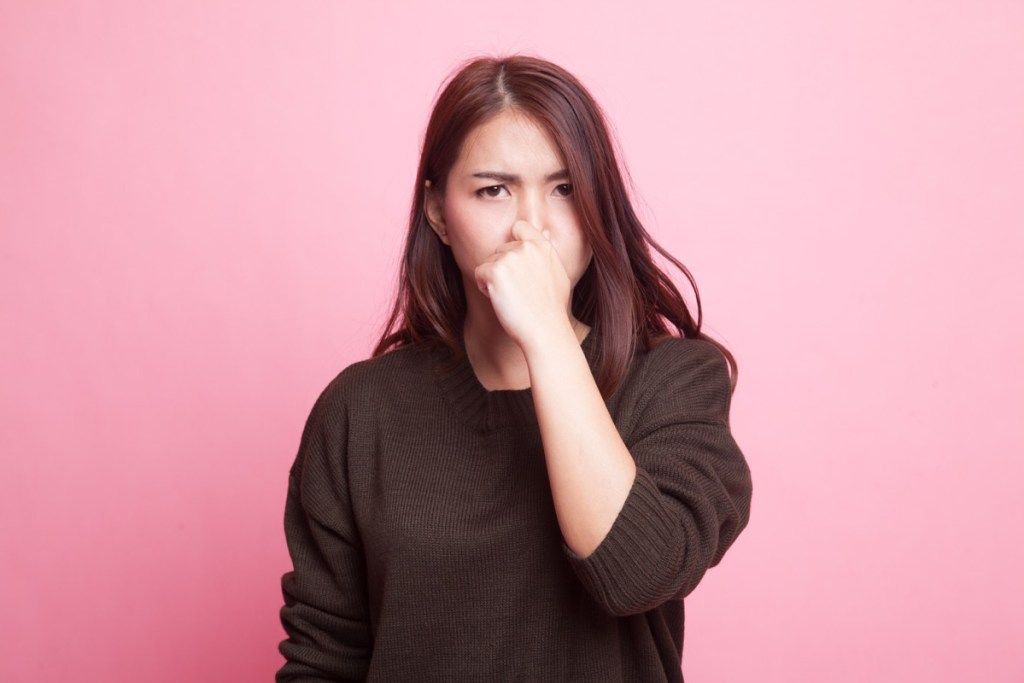 Giovane donna asiatica tenendo il naso a causa di un cattivo odore su sfondo rosa - Immagine