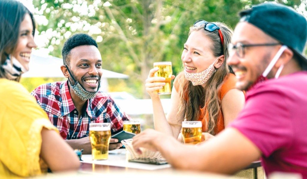 دوستوں نے کھلے ہوئے چہرے کے ماسک کے ساتھ بیئر پیتے ہوئے - شراب نوشی والے بار میں خوشی کے وقت بات کرنے میں لوگوں کے ساتھ تفریح ​​کرنے کے ساتھ نیا عام طرز زندگی کا تصور۔