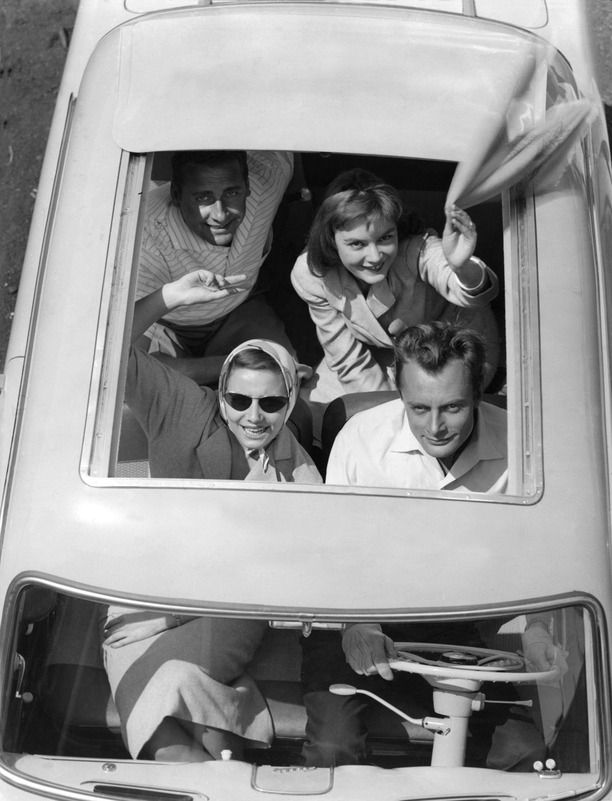 1950 년대 오픈 컨버터블 자동차 위에서 손을 흔드는 젊은이들