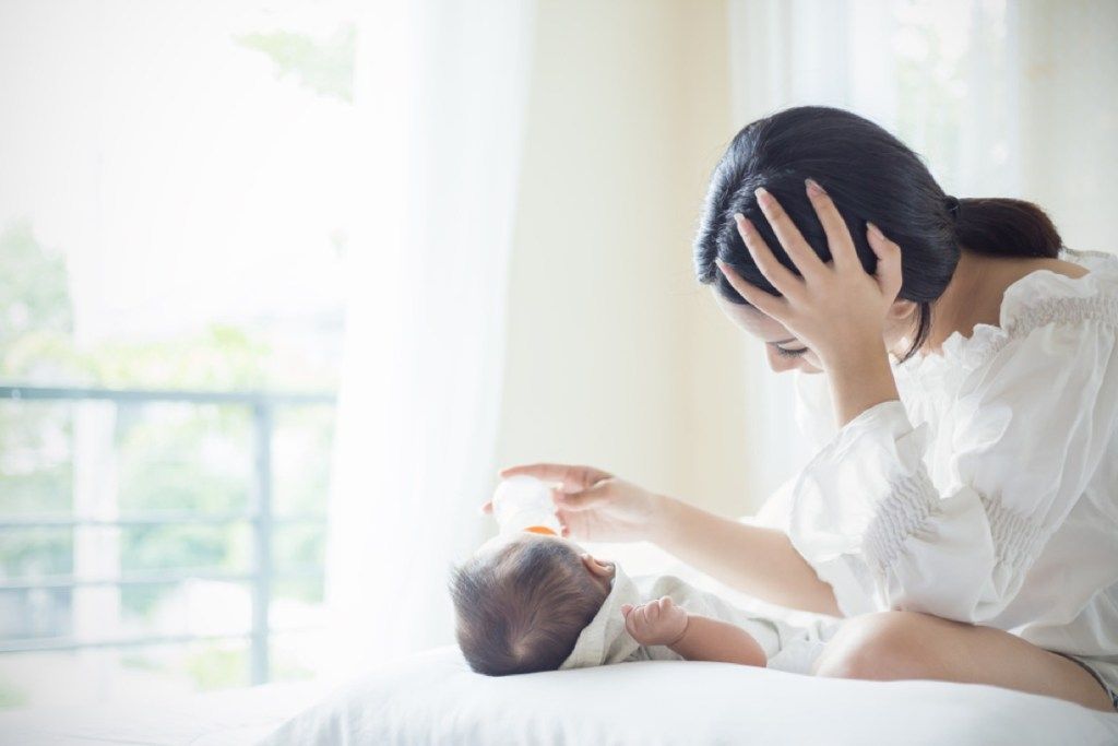 Mujer mirando deprimida mientras alimenta al bebé, mamá trabajadora