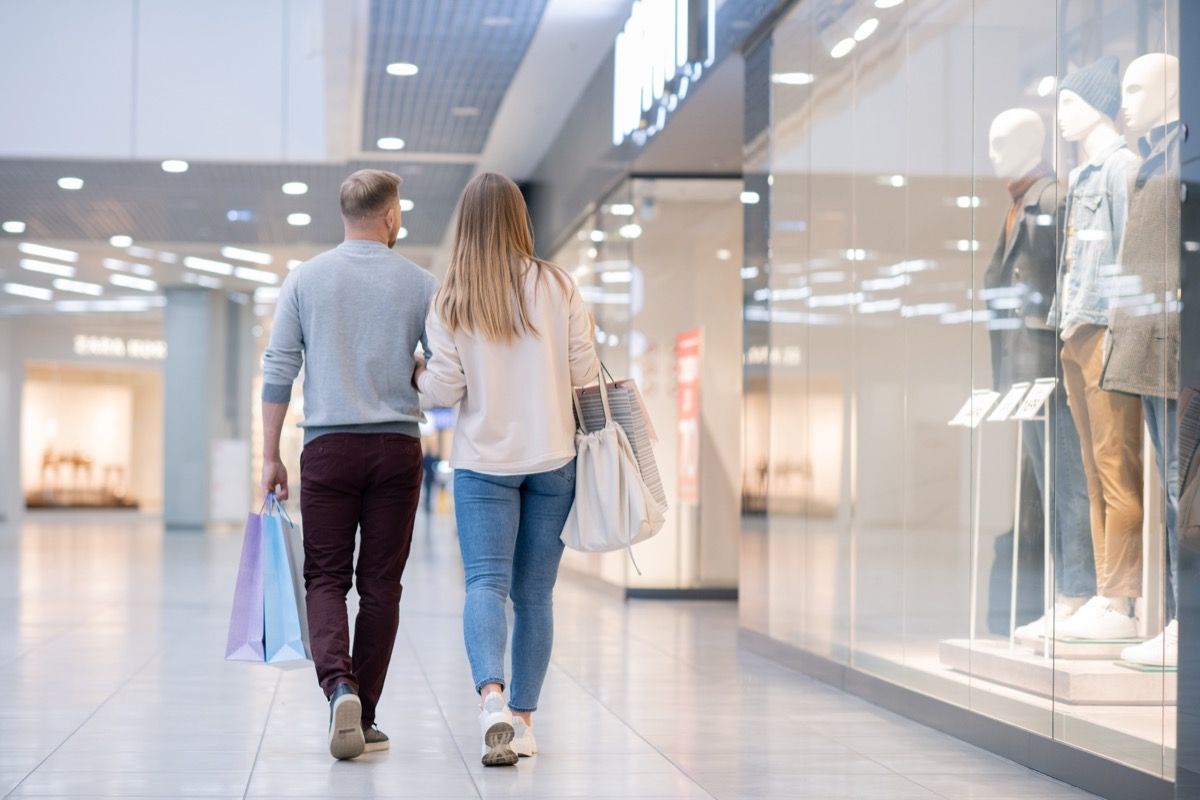 Pogled straga na mladi slučajni par koji se kreće duž izloga u tržnom centru dok ga napuštaju nakon kupnje onoga što su željeli