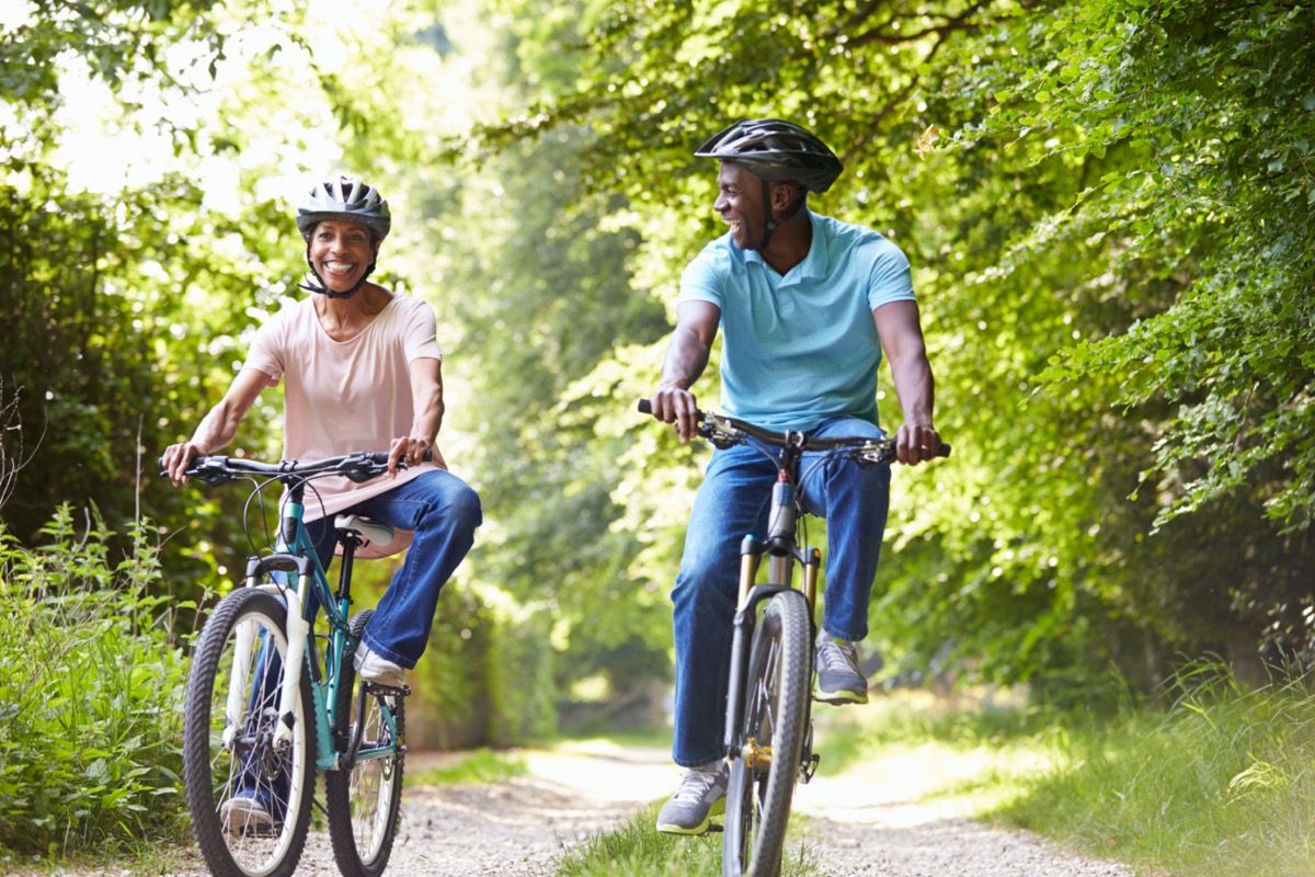 Femme noire mature en chemise rose et homme en chemise bleue à vélo