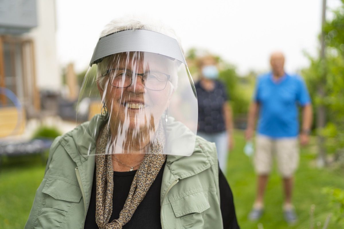 äldre vit kvinna som ler bakom en ansiktssköld utanför