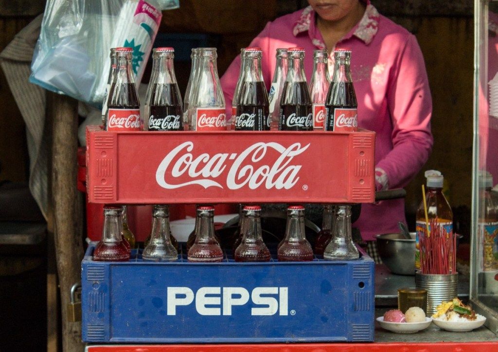 नोम पेन्ह, कंबोडिया- 02 जनवरी, 2014. कोका-कोला और पेप्सी की बोतलें प्लास्टिक कंटेनर में ढेर हो गईं - विंटेज शैली। सभी समय के सबसे बड़े व्यापारिक प्रतिद्वंद्वियों में से एक का प्रतीकात्मक प्रतिनिधित्व। - छवि