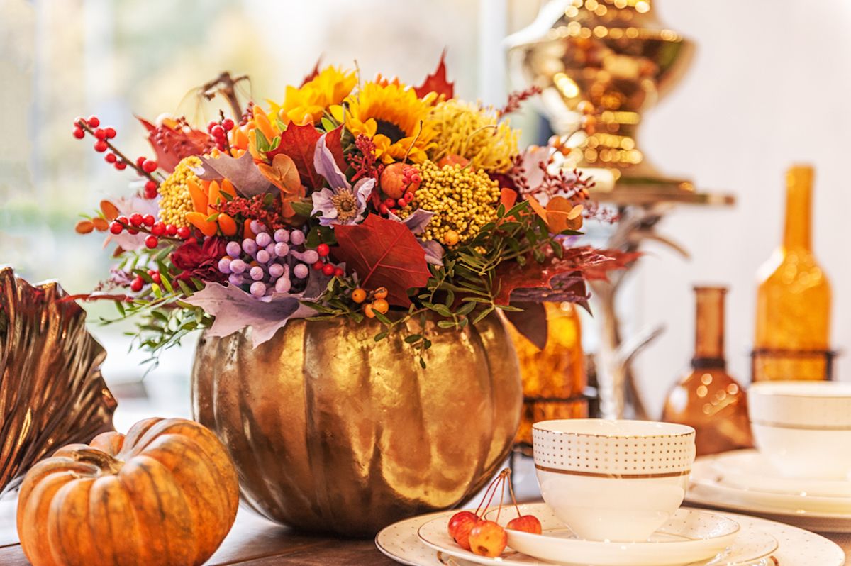 Composición de flores de otoño en un jarrón de calabaza sobre una mesa decorada con calabazas