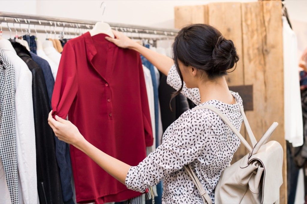 seorang wanita memeriksa atasan merah di toko pakaian