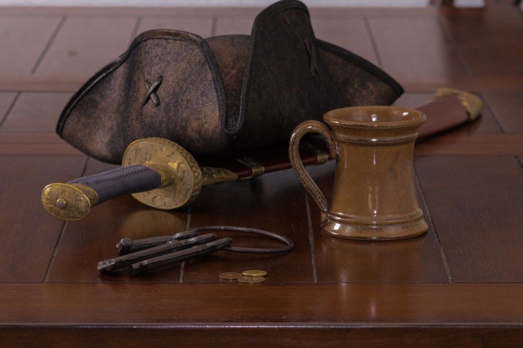 chapéu de pirata e caneca na mesa com espada