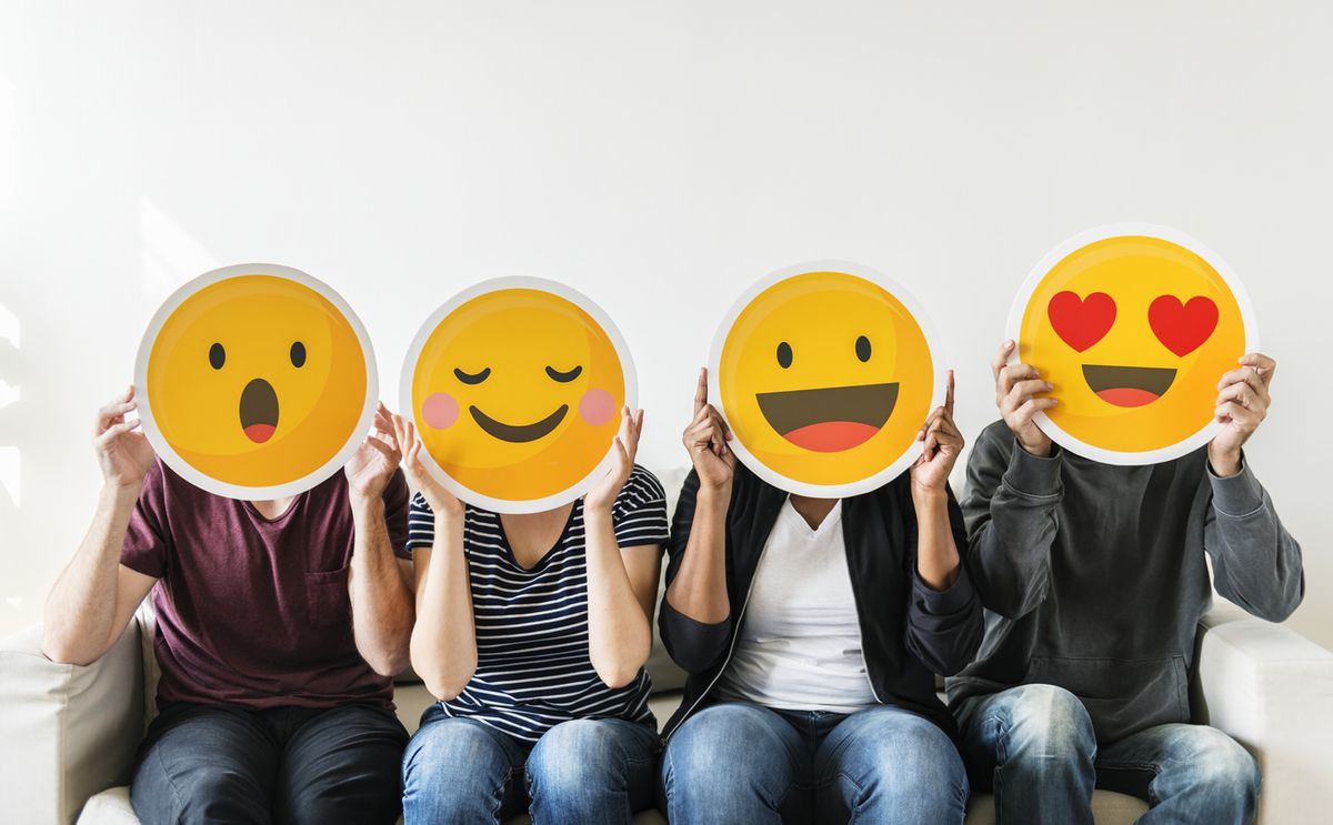 Patru persoane așezate pe o canapea, fiecare ținând câte un emoji de reacție diferit tăiat în fața fețelor.
