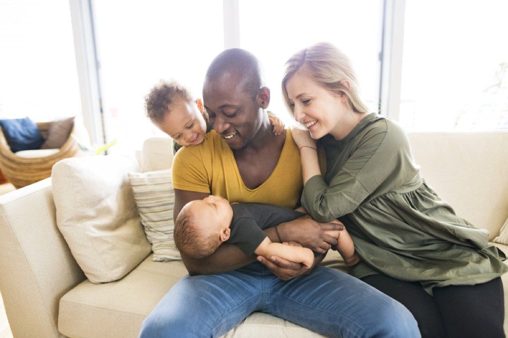 hvit mor og svart far med blandet rase småbarn og spedbarn som sitter på sofaen