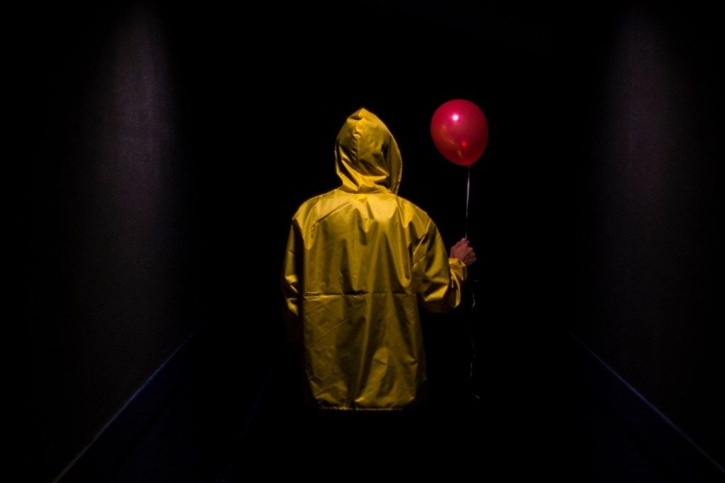 Gelbe Kapuzenfigur mit rotem Ballon im dunklen gruseligen Korridor