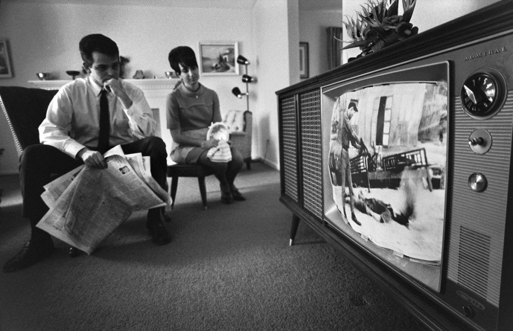 Hombre y mujer de la década de 1960 ven televisión en la vida, sentados en sillas, él tiene un periódico, la vida antes de la tecnología hechos de la boda real