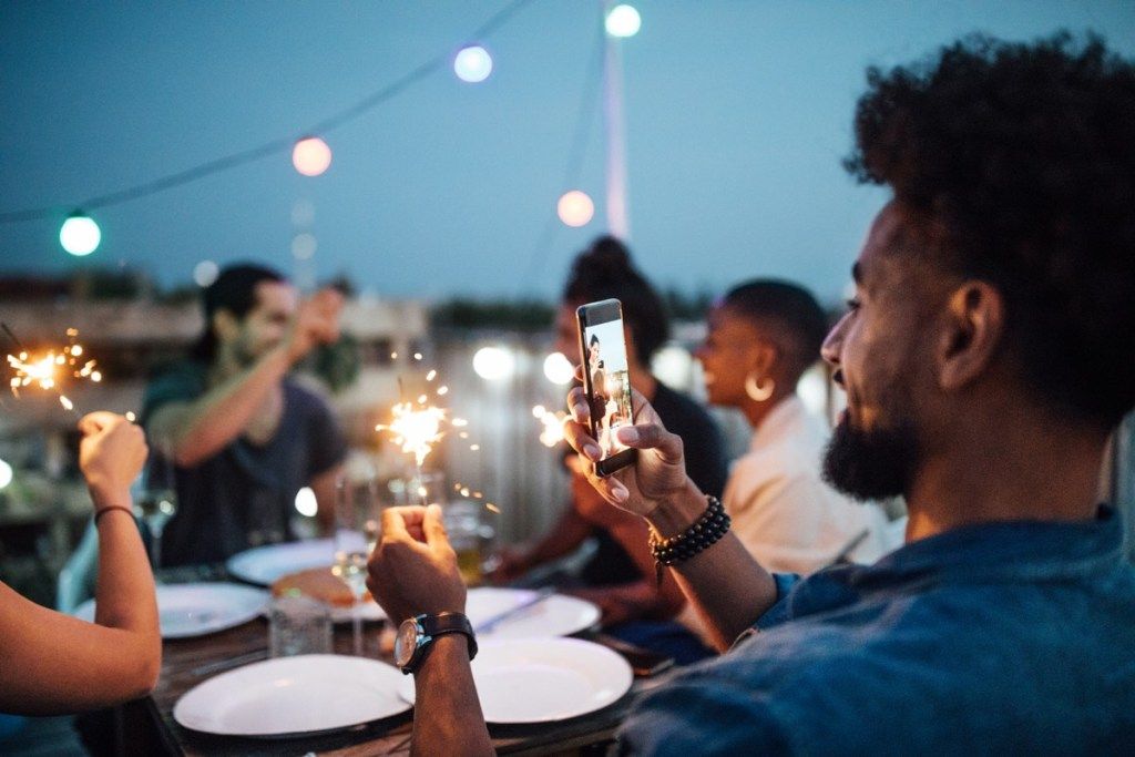 vīrietis fotografē dzirksteles ballīti savā telefonā