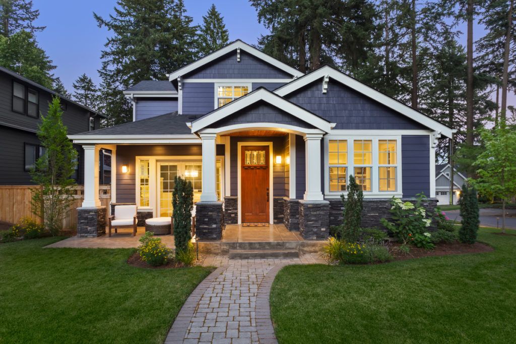 fasada temno modrega doma z urejenim travnikom, urejanjem okolice in ozadjem dreves