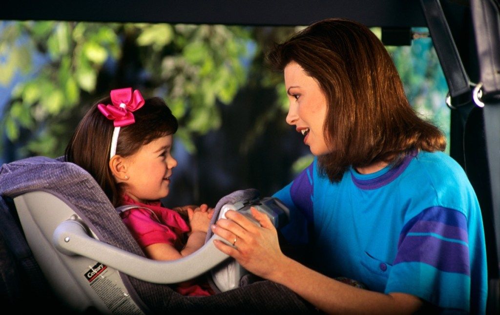 Mãe amarrando a filha em um assento de carro nos anos 90