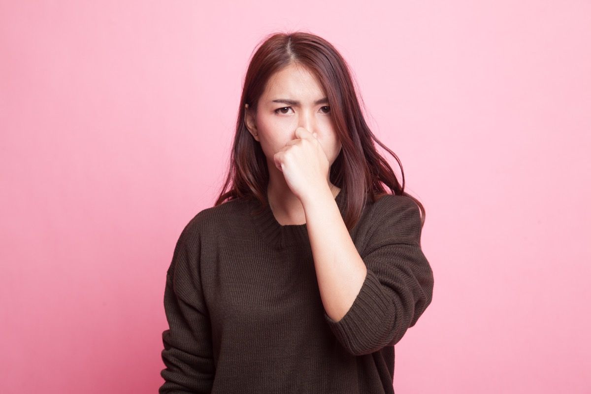 Joven asiática tapándose la nariz debido a un mal olor sobre fondo rosa - Imagen
