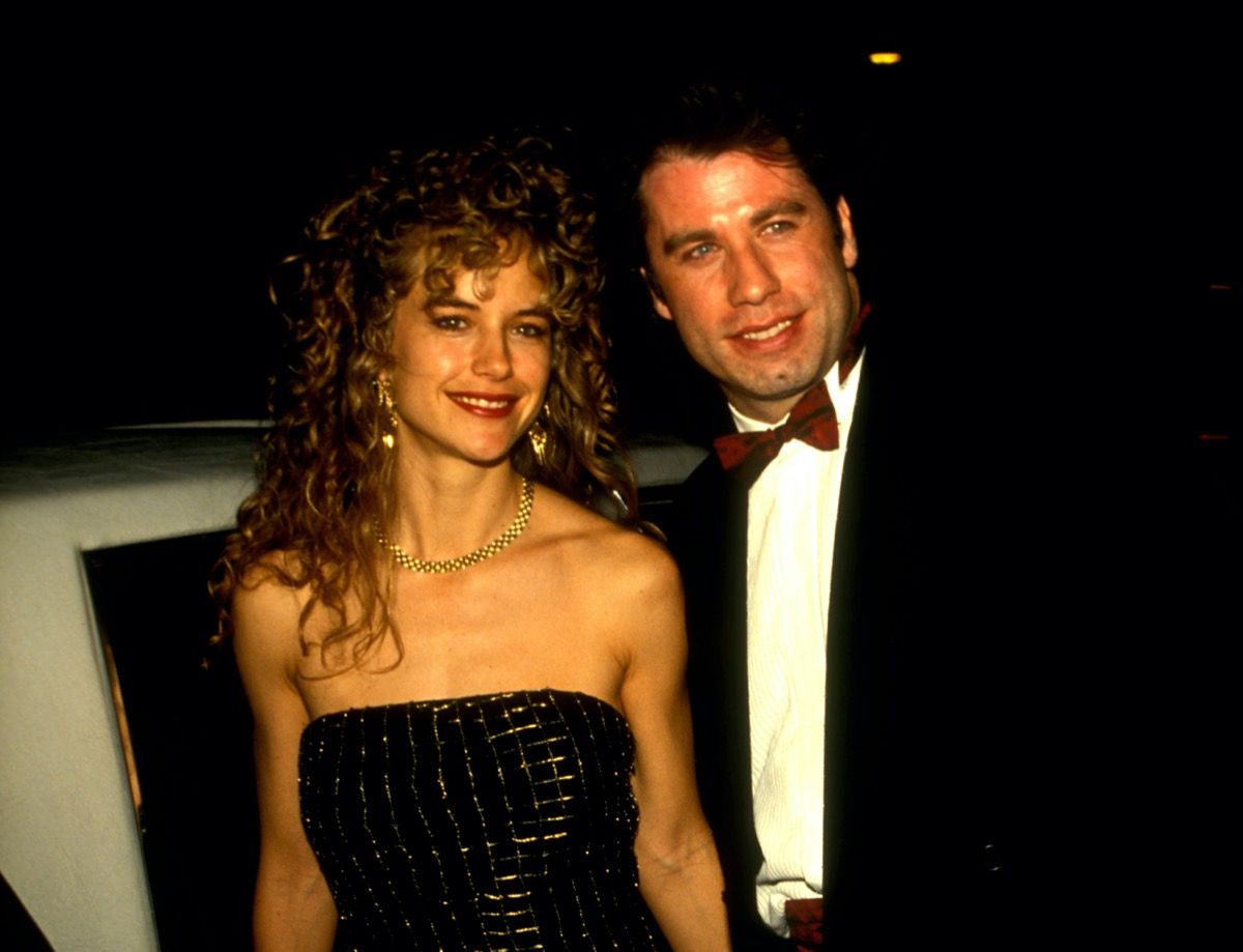 John Travolta สวมสูทสีดำและเสื้อเชิ้ตสีขาวส่วน Kelly Preston สวมชุดสีดำนอกร้านอาหารในปี 1991