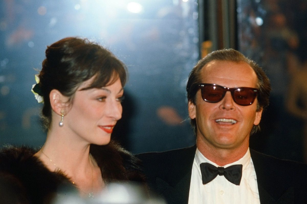 Anjelica Huston สวมเสื้อคลุมสีดำและ Jack Nicholson สวมชุดสูทสีดำที่ American Film Institute Gala Tribute to John Huston ในปี 1983