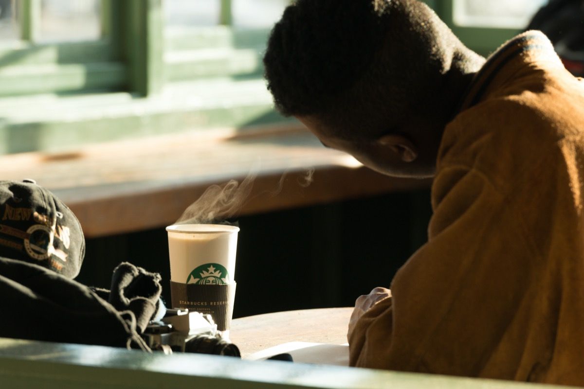 Vyras Pike Place turguje vėlyvą dieną su karštu puodeliu „Starbucks“ kavos.