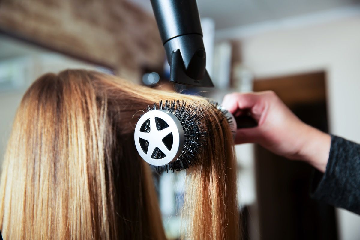 Thợ làm tóc chuyên nghiệp cho phụ nữ làm kiểu tóc bằng máy sấy tóc cho phụ nữ trẻ trong thẩm mỹ viện.
