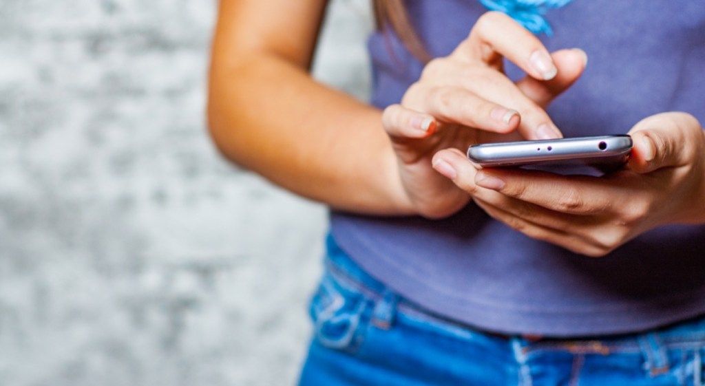 युवा किशोरी लड़की मोबाइल फोन या स्मार्टफोन का उपयोग ग्रे वॉल बैकग्राउंड पर करती है