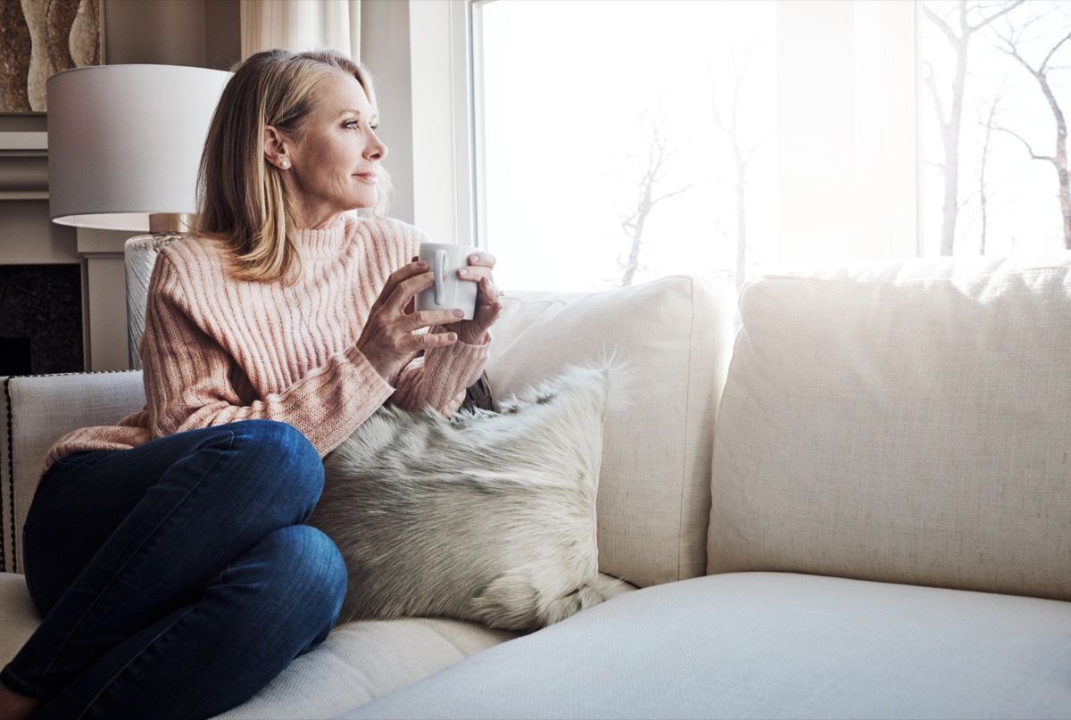 nainen istuu yksin sohvalla siemaillen kahvia