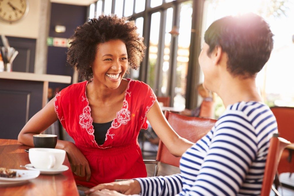 Dvi draugės moterys kalba kavinėje