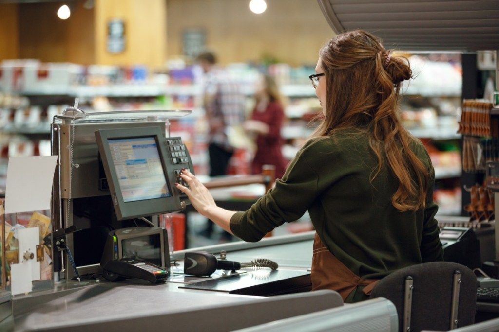 giovane donna bianca operante registratore di cassa al negozio di alimentari