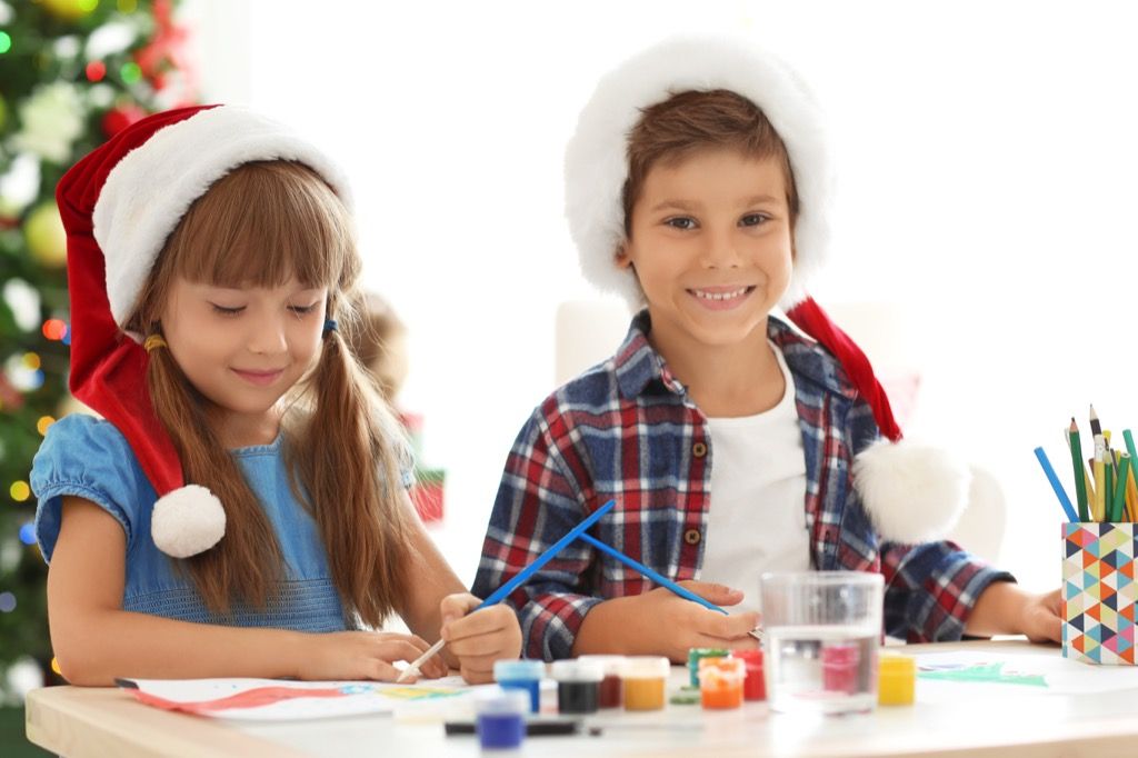 Mažas berniukas ir mergaitė, dėvintys Kalėdų senelio kepures ir dirbantys amatą