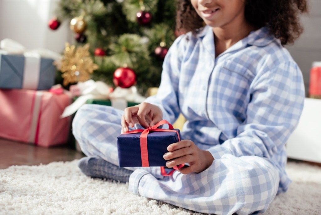 Liten jente som åpner julegaver i pyjamas