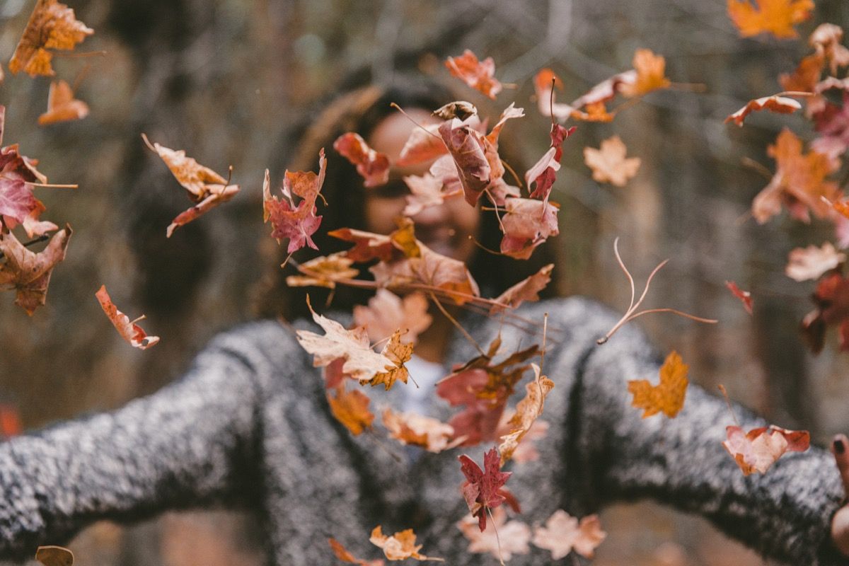 Mujer arrojando hojas de otoño crujientes en el aire clima de otoño salud