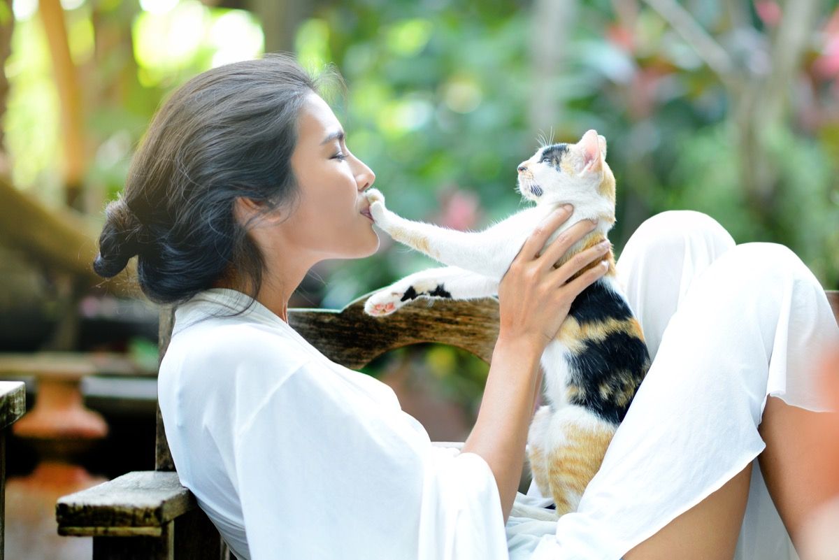 युवा महिला बगीचे में आरामकुर्सी पर एक बिल्ली के साथ आराम कर रही है