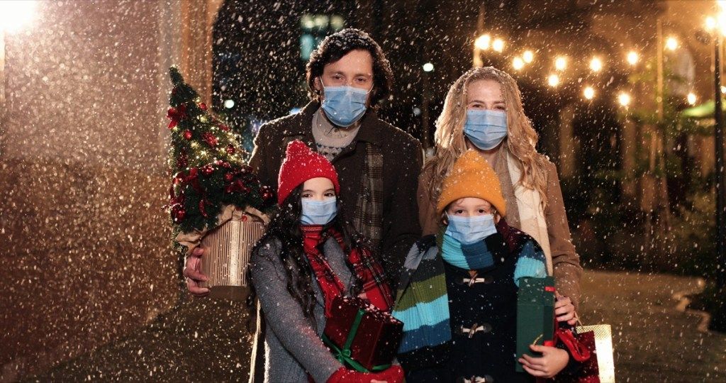 мъж, жена и деца носят маски навън в снега и държат коледни подаръци