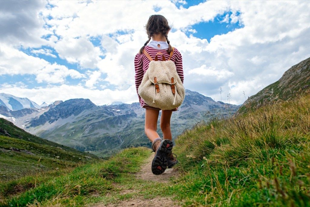 Gadis kecil berjalan di laluan gunung semasa lawatan. dengan beg galas. - Imej