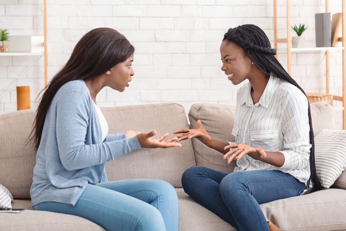 dvi juodos moterys sėdi ant sofos ir ginčijasi tarpusavyje
